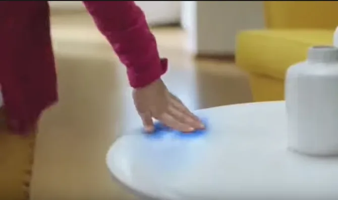 Fotogramma di una pubblicità TV di un disinfettante: una mano poggia su un tavolino bianco lasciando un alone luminoso azzurro a indicare la zona "pulita".